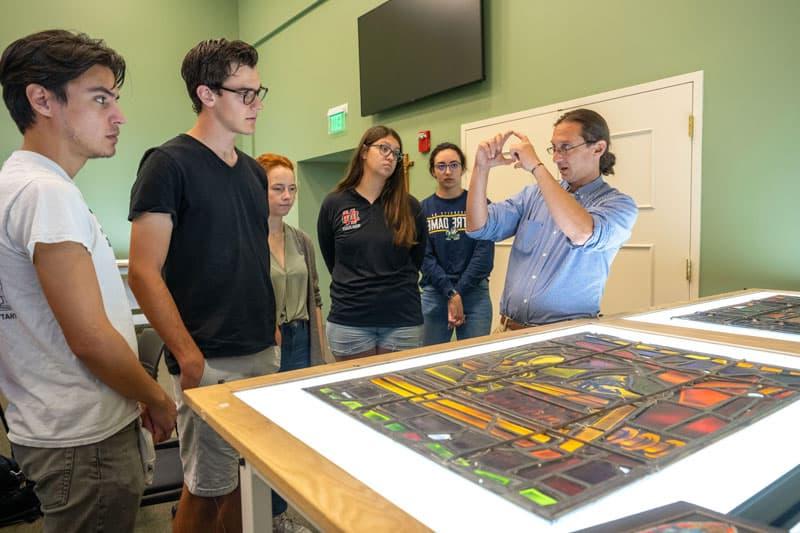 Professor Stephen Hartley explains to students the process of light transfer through glass in front of the mock up panels of Gutenberg on the Press made for the “Protestant Stream of Christianity” window designed by 查尔斯·Z. 劳伦斯在华盛顿特区的国家大教堂.